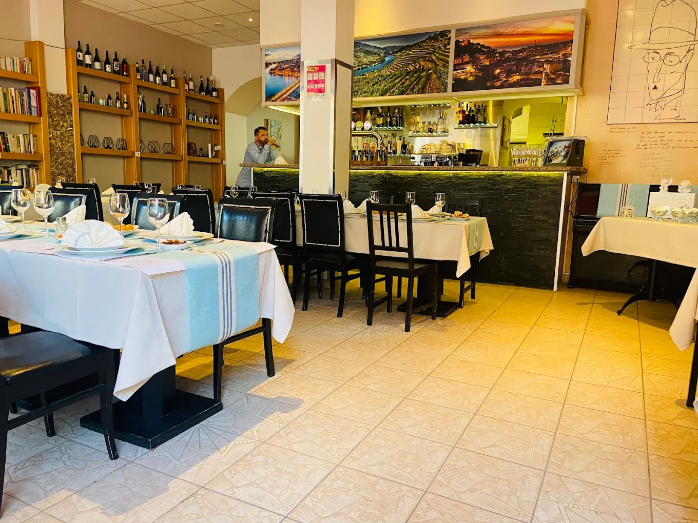 La salle du restaurant Pessoa : tables dressées, bibliothèque de livres et photographies de la vallée du Douro, Genève.