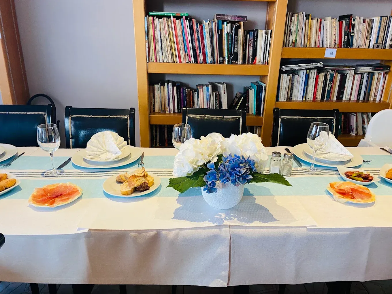 Table dressée au restaurant Pessoa, nappe blanche et bleue, hortensias et étagères de livres en fond.